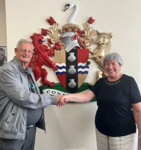 Cllr Russell Goodchild and Cllr Madeline Russell Shaking Hands in front of Bedfordshire Crest